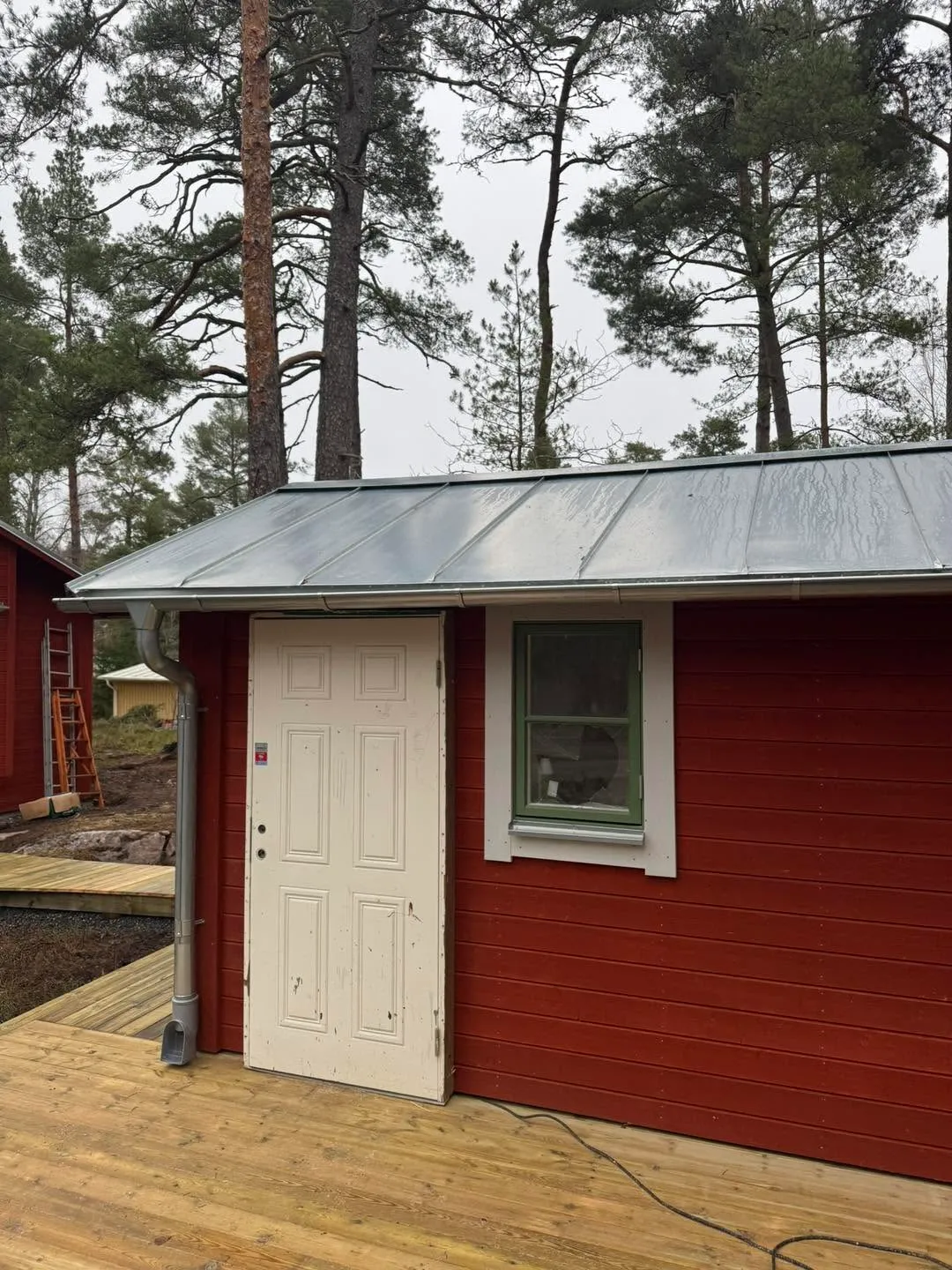 Röd stuga med plåttak och trädäck