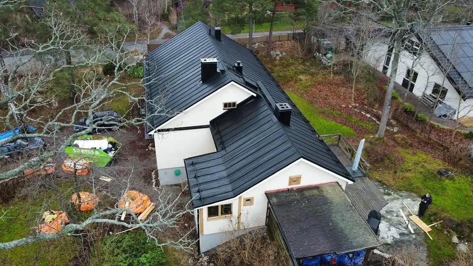 Flygbild över hus med mörkt plåttak vid vattnet